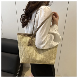 Close-up of woven straw tote bag with brown leather handles worn by a model