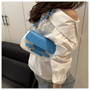 Detalle de bolso bandolera de cuero azul y blanco con hebillas doradas y cadena acrílica