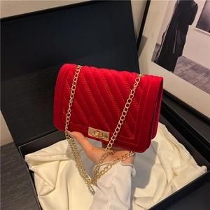 Red velvet crossbody bag with V-shaped quilting and gold metal lock on a silk background