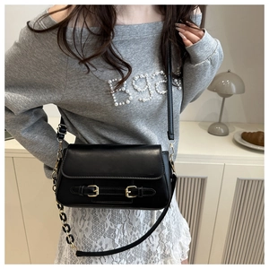 Detail of black leather shoulder bag with golden buckles and chain strap on model