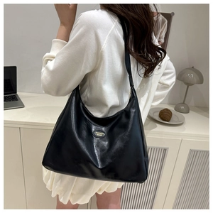 Detail of a black glossy PU leather shoulder bag with gold oval fashion logo plaque