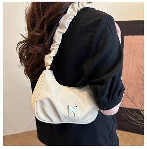 Detail of off-white pleated shoulder bag with 3D butterfly accessory on canvas texture