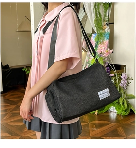 Détail du sac bandoulière en toile noire avec sangle réglable et étiquette de marque