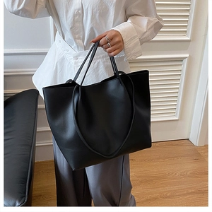 Detailed close-up of a large black matte tote bag held by a model in a minimalist setting