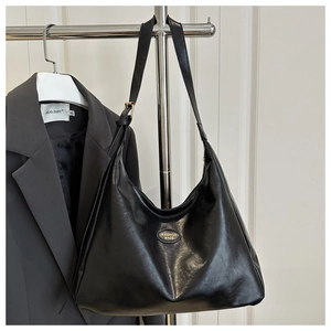 Detail of black glossy synthetic leather messenger bag with golden oval logo plaque