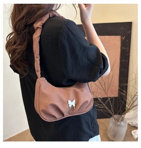 Detail of a crescent-shaped underarm bag featuring pleated fabric and a butterfly buckle