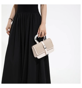 Detail showing u-shaped metal handle on cream leather and woven textured square handbag