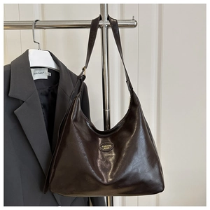Detailed view of deep brown leather tote with a gold-tone logo on an office suit background