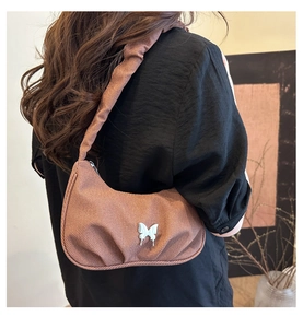 Détail de la texture d'un sac demi-lune marron avec un ornement papillon en métal argenté