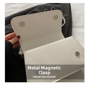 Detail of the white shoulder bag featuring a durable metal magnetic buckle closure