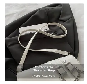 Detail of white baguette bag featuring silver buckles and chains on dark blazer