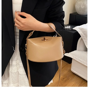 Detail view of the elegant metal twist lock and litchi texture on the beige bucket bag