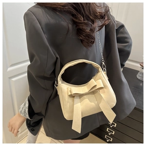 Detail of cream bow shoulder bag with metal chain strap shown on model's side