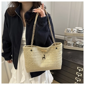 Detail of woven straw tote bag featuring gold chain strap and deer pendant charm
