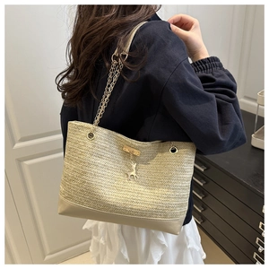 Close-up of woven straw tote bag featuring gold chain strap and metal deer charm detail