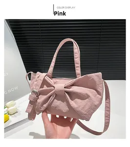 Pink bow-shaped handbag in washed fabric held by hand with long adjustable strap