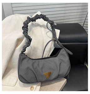 Close-up of grey textured handbag featuring scrunchie handle and gold triangle plaque
