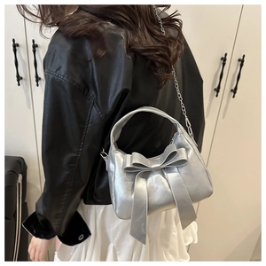 Detail of silver metallic handbag featuring large bow decoration and chain strap on a model