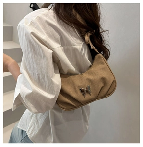 Sac sous le bras en velours côtelé marron avec décoration papillon porté par un modèle