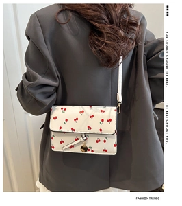 Close-up of white leather crossbody bag with cherry pattern and gold charm on a grey blazer