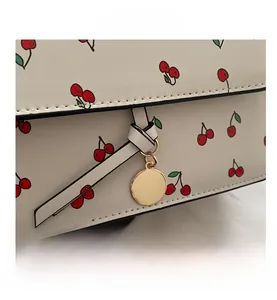 Close-up of cherry pattern handbag with golden metal pendant and high-quality PU leather