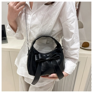 Détail du sac en cuir brillant noir avec nœud décoratif et bandoulière en chaîne argentée