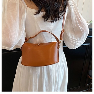 Brown semi-circular leather crossbody bag with gold hardware shown on a model