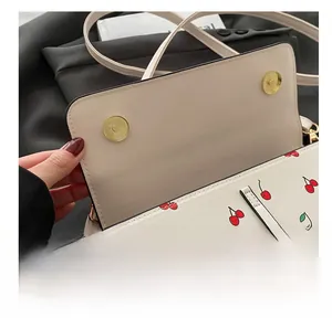 Detail showing the magnetic hardware buckles and cherry print on the cream crossbody bag