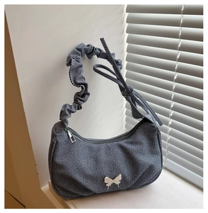 Detail of blue denim shoulder bag featuring a silver butterfly charm and ruched strap