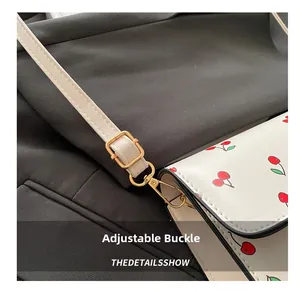 Close-up of adjustable golden metal buckle and leather strap on a cherry pattern handbag
