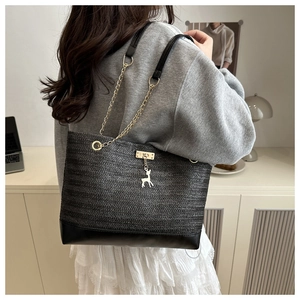Detailed shot of black woven straw tote featuring gold deer charm and leather chain strap