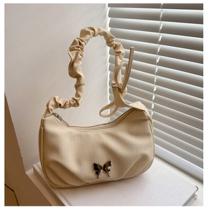 Detail of cream pleated shoulder bag featuring a silver butterfly charm and zipper