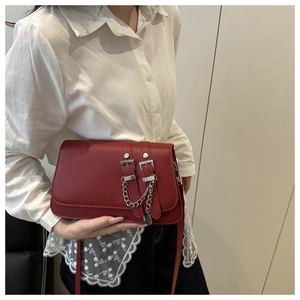 Detail of burgundy rectangular shoulder bag with silver buckles and chain decoration