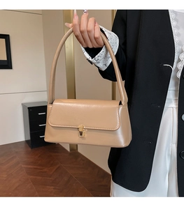 Detail of khaki vintage baguette bag with gold metal clasp held by a model in a blazer
