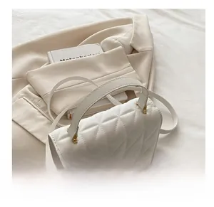 Detail view of white quilted crossbody bag with gold lock on beige blazer background