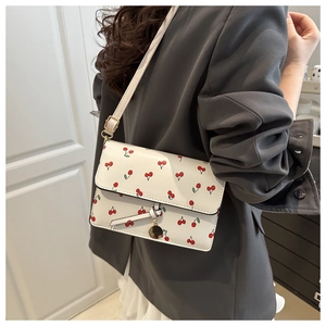 Detail of white leather shoulder bag with red cherry print and gold charm pendant