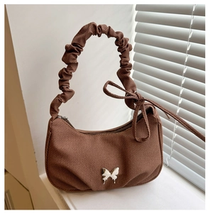 Detail of a brown ruched fabric shoulder bag featuring a silver metal butterfly ornament