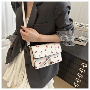 Close-up of a white cherry print shoulder bag worn with a blazer and pleated skirt