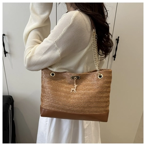 Close-up of woven straw tote bag with leather base, gold chain, and deer charm