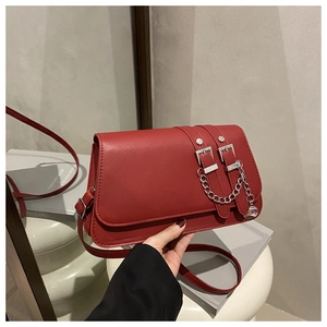 Detail of red faux leather handbag featuring silver double metal buckles and chain charms
