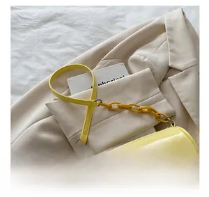 Détail d'un sac cylindrique jaune sur un blazer beige avec une bandoulière à chaîne mate
