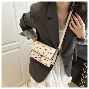 Close-up of a white leather crossbody bag with cherry prints worn with a gray blazer