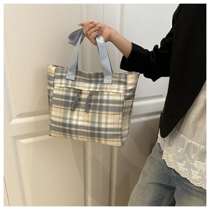 Detail of plaid tote bag with blue handles and decorative drawstring on canvas