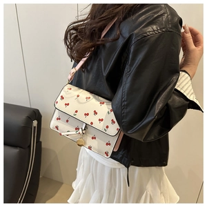 Detail of white cherry print handbag with gold metal charm and pink shoulder strap