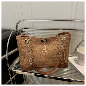 Close-up of woven straw tote bag with gold deer pendant and chain leather strap