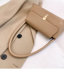 Détail d'un sac baguette kaki avec fermoir doré posé sur un trench-coat élégant
