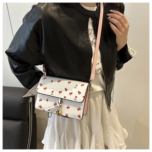 Detail of white crossbody bag with red cherry prints and decorative metal pendant