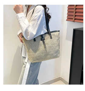 Détail d'un grand sac cabas en paille avec anses en cuir noir porté à l'épaule