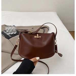 Detail of caramel leather handbag featuring gold twist lock and smooth crescent shape