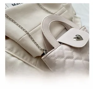 Detail einer beigen Stepptasche mit herzförmigem Metallschloss und silbernem Kettenriemen